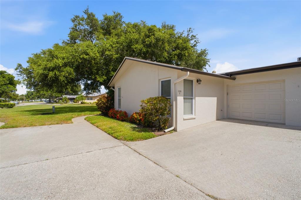 A beige single-story house exterior features a concrete driveway, a garage, and a large tree — 1335 QUEEN ANNE DRIVE UNIT C, PALM HARBOR, FL