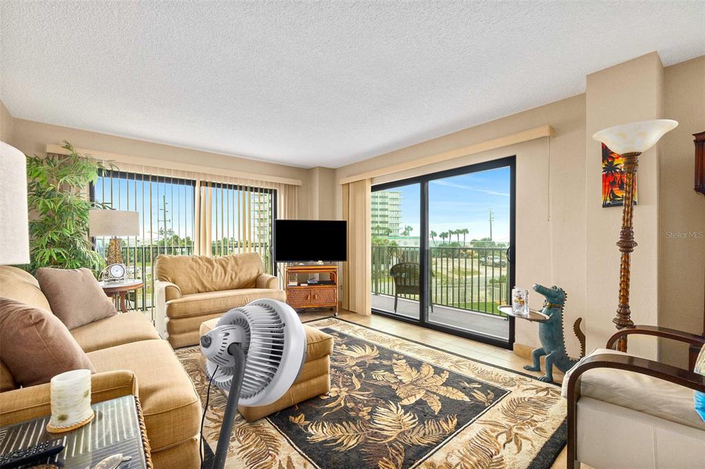 A living room features tan furniture, a tropical area rug, and sliding glass doors to a balcony — 3600 S OCEAN SHORE BOULEVARD UNIT 211, FLAGLER BEACH, FL