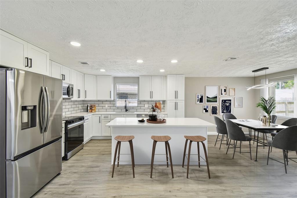 A modern kitchen features white cabinetry, a central island with bar stools, and dining area — 2258 GEORGE WYTHE ROAD, ORANGE PARK, FL