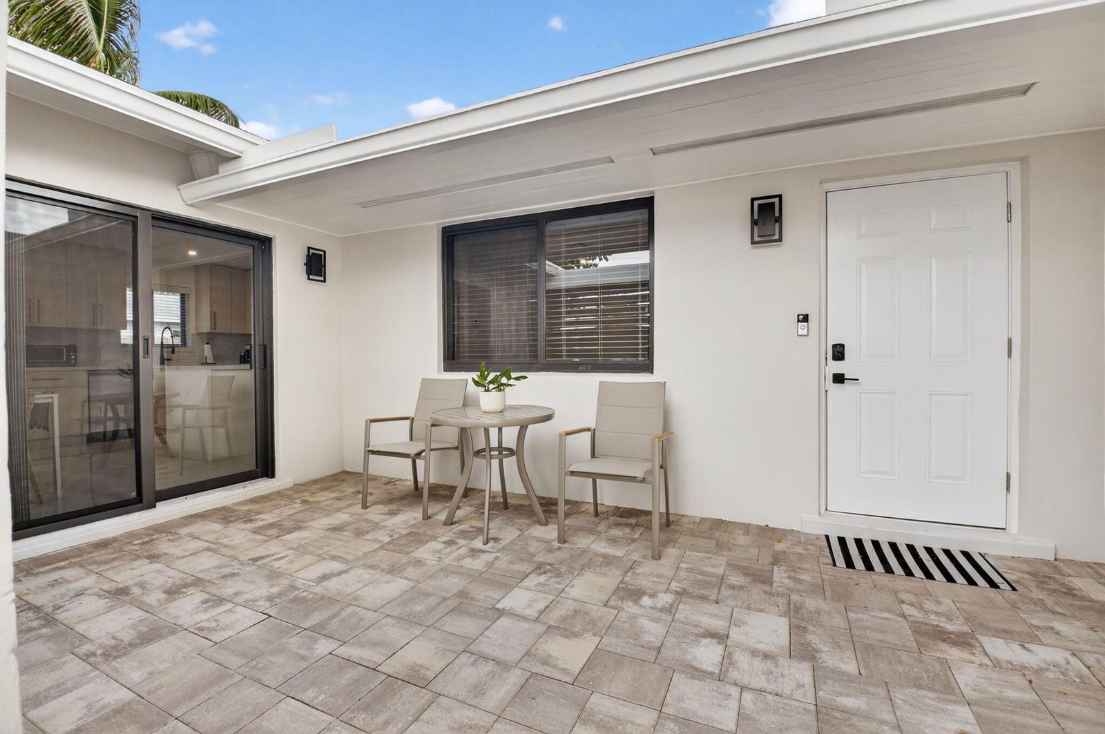 A paved patio features a small bistro set, a sliding glass door, and a white door — 513 Lindell Boulevard, Delray Beach FL 33444, DELRAY BEACH, FL