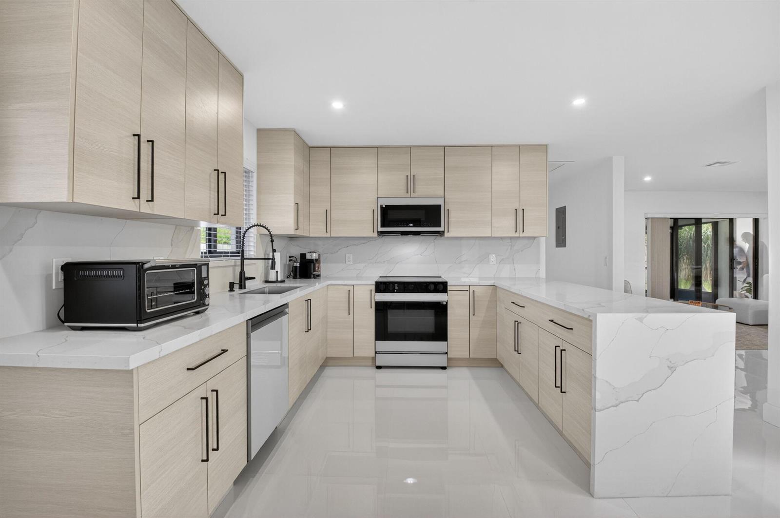 A modern kitchen features light wood cabinets, white marble countertops, and stainless steel appliances — 513 Lindell Boulevard, Delray Beach FL 33444, DELRAY BEACH, FL