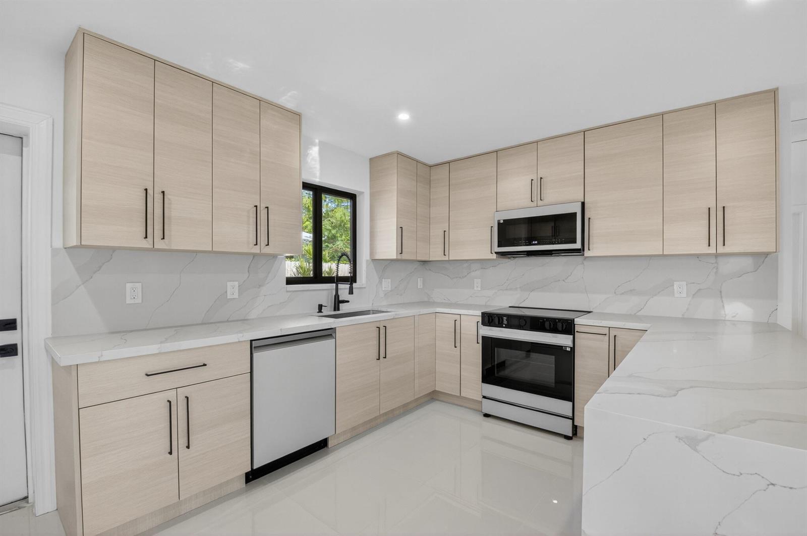 A modern kitchen features light wood cabinets, white marble-patterned countertops, and stainless steel appliances — 513 Lindell Boulevard, Delray Beach FL 33444, DELRAY BEACH, FL