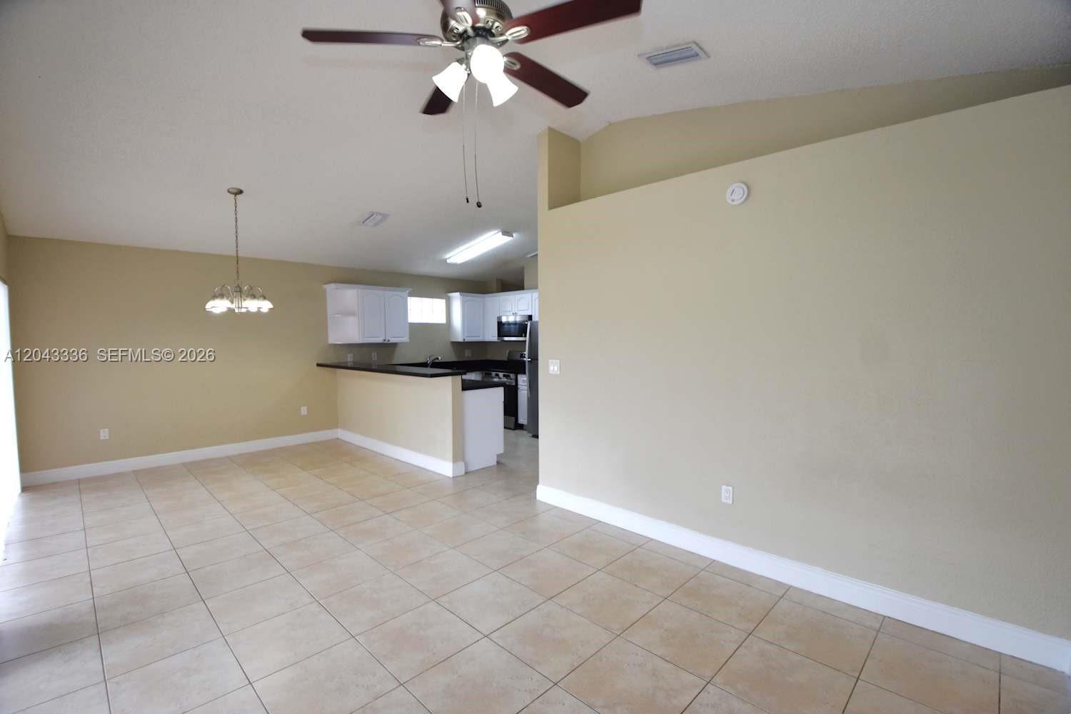 An open-concept kitchen with white cabinets and a breakfast bar overlooks a tiled dining area — HIALEAH, FL