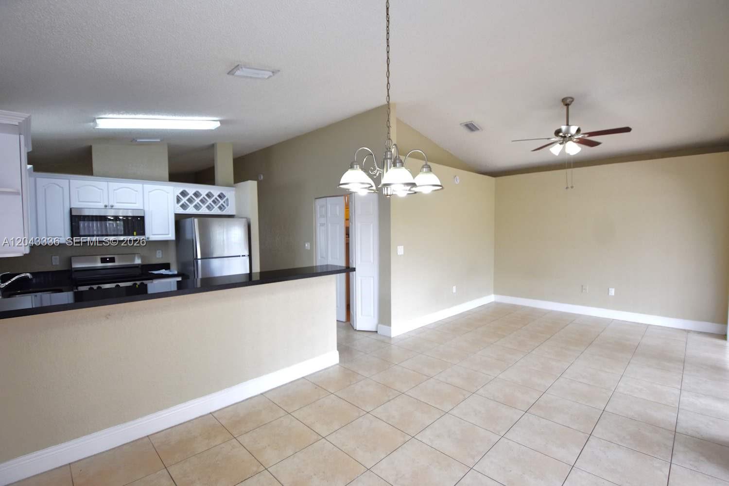 A kitchen with white cabinets and a breakfast bar opens into a tiled dining area — HIALEAH, FL