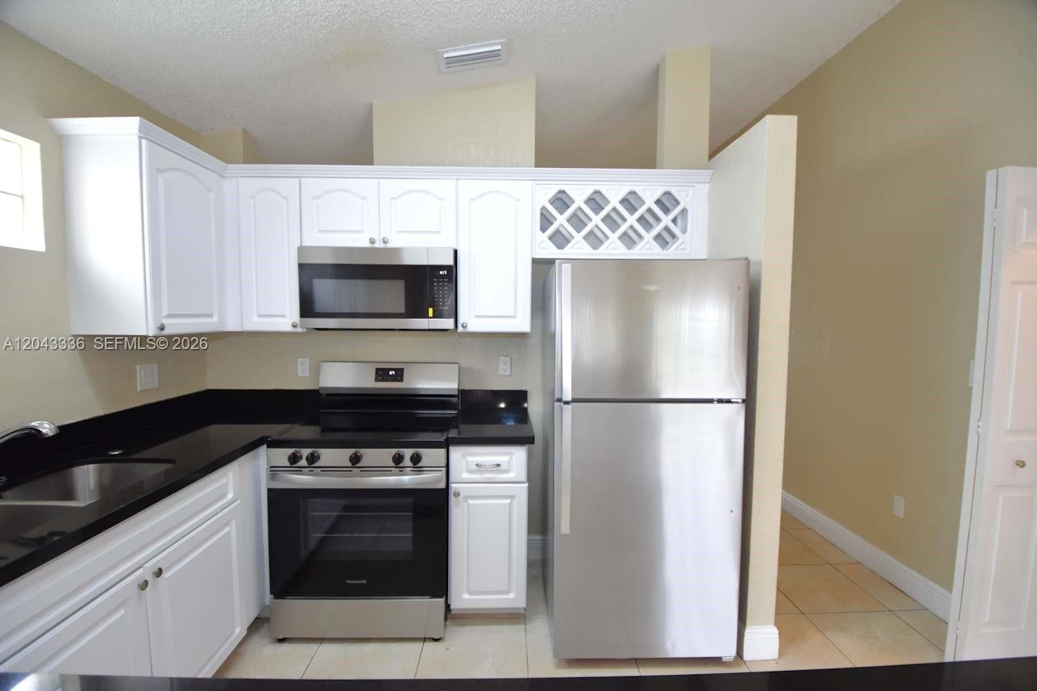 A kitchen features white cabinets, stainless steel appliances, and black countertops — HIALEAH, FL