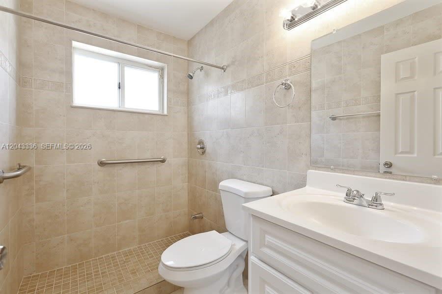 A bathroom features beige tiled walls, a walk-in shower, a white vanity, and a toilet — HIALEAH, FL