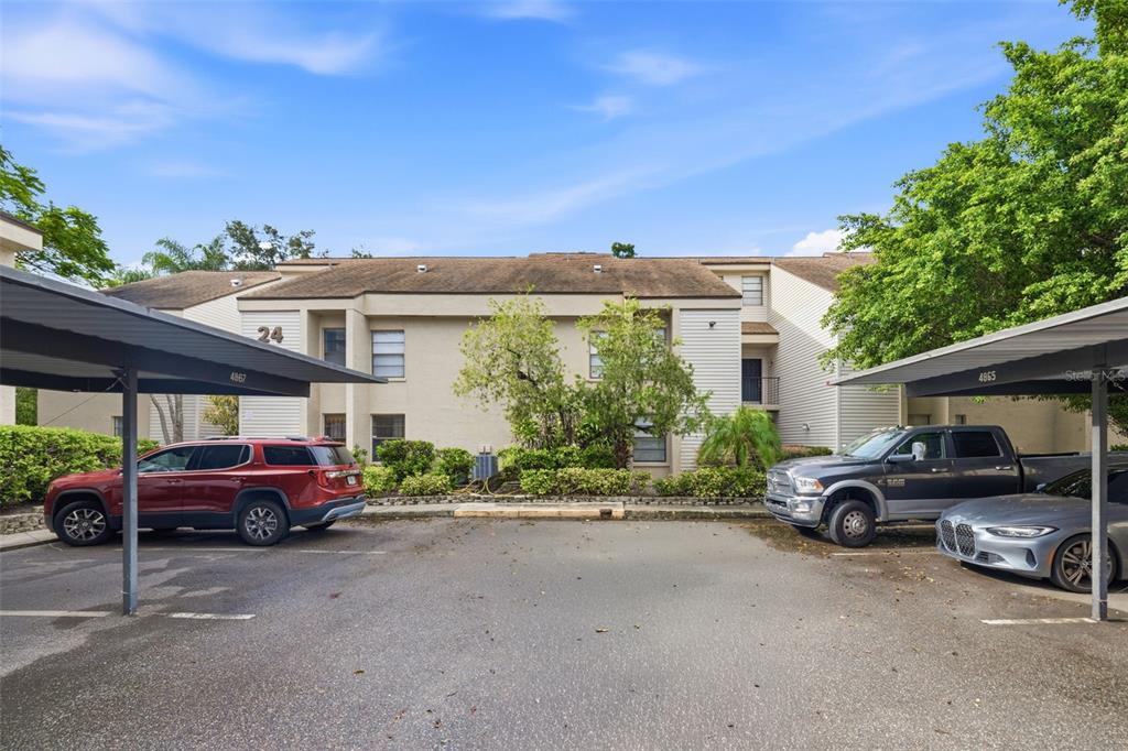 A two-story apartment building exterior with covered parking spaces and parked vehicles in front — 4873 PURITAN CIRCLE UNIT 2401, TAMPA, FL