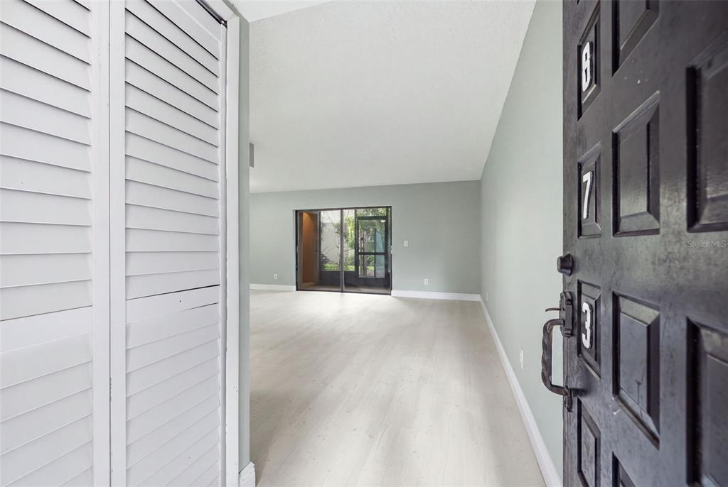 An entryway leads into a living room with light wood floors and a screened patio — 4873 PURITAN CIRCLE UNIT 2401, TAMPA, FL