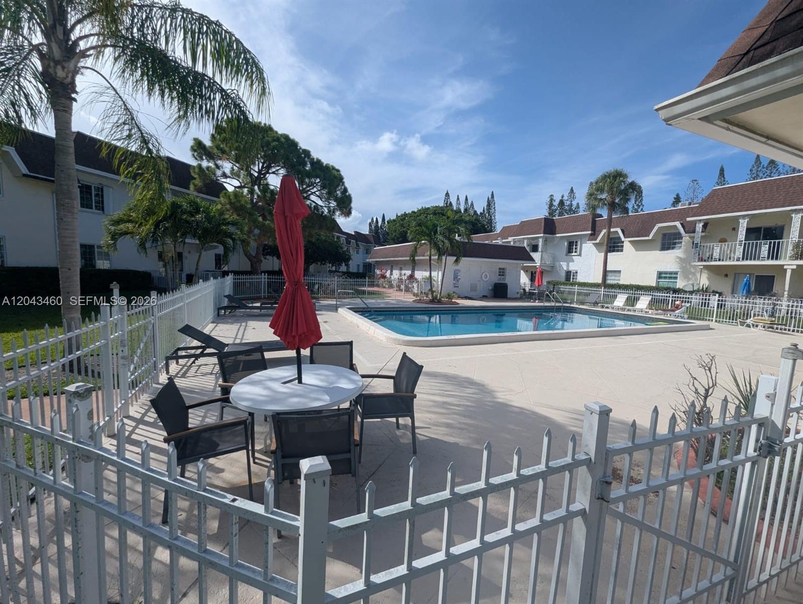 A swimming pool area features a patio with a table, chairs, and a red umbrella — 700 SE 2nd Ave # 313, Deerfield Beach FL 33441, DEERFIELD BEACH, FL