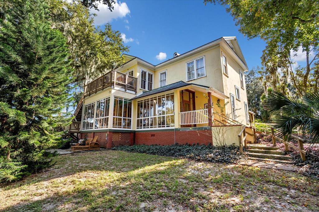 A two-story yellow house with a screened-in porch, brick foundation, and a wooden balcony — 620 N TUBB STREET, OAKLAND, FL
