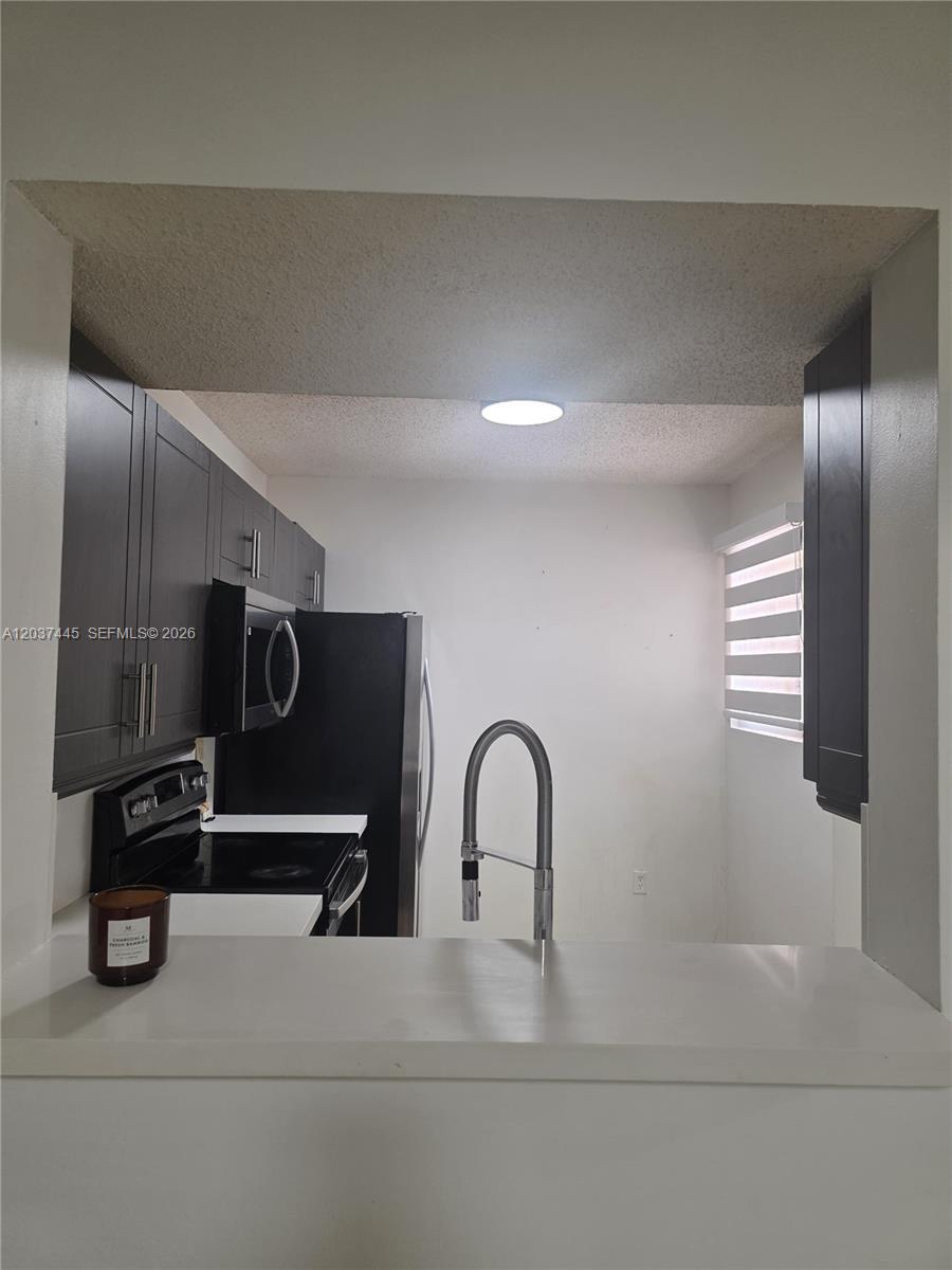 A kitchen features dark cabinets, black appliances, and a pass-through window with a counter — 15711 SW 137th Ave # 101, Miami FL 33177, MIAMI, FL