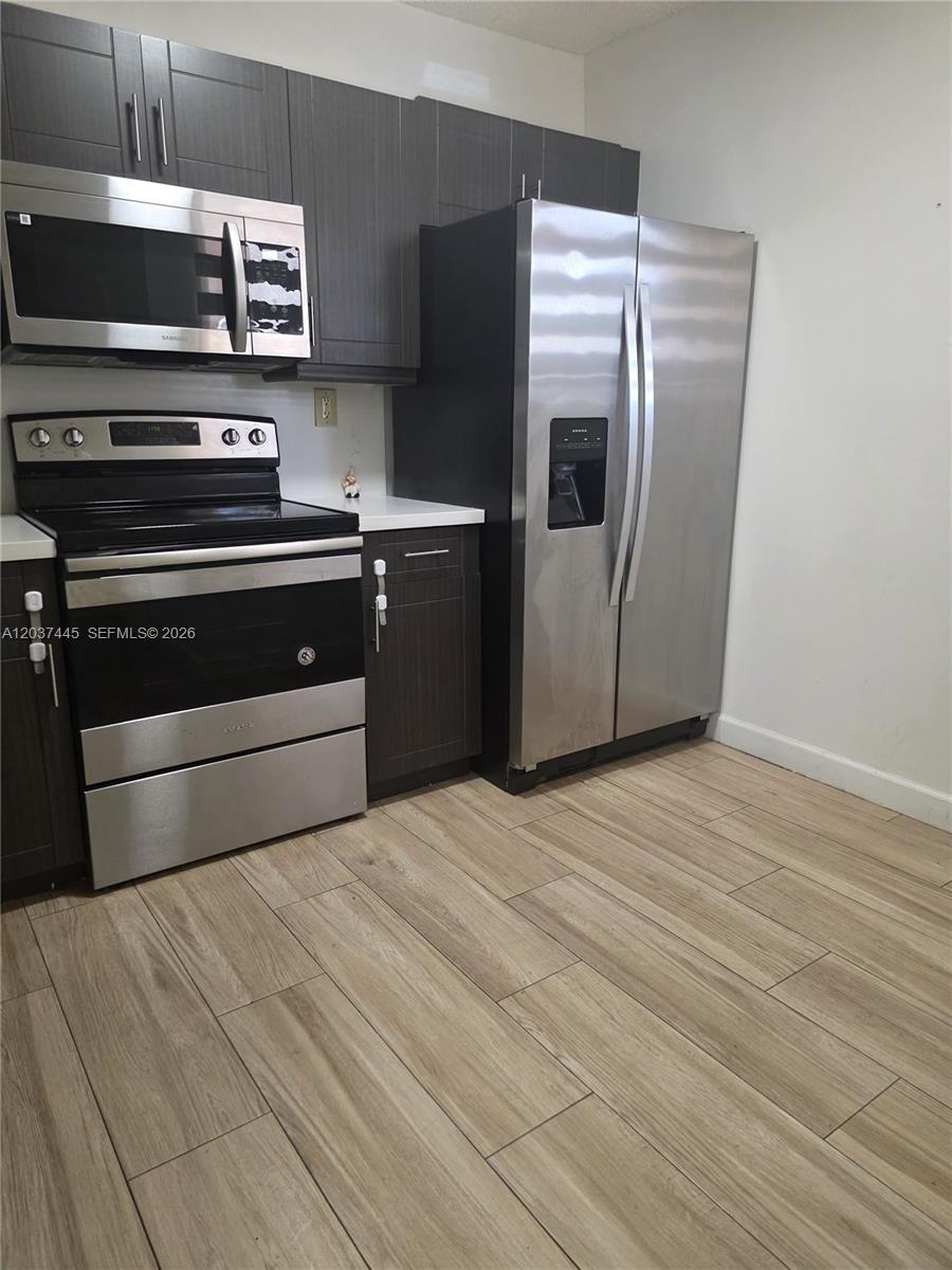 A kitchen features dark wood cabinets, stainless steel appliances, and light wood-look tile flooring — 15711 SW 137th Ave # 101, Miami FL 33177, MIAMI, FL
