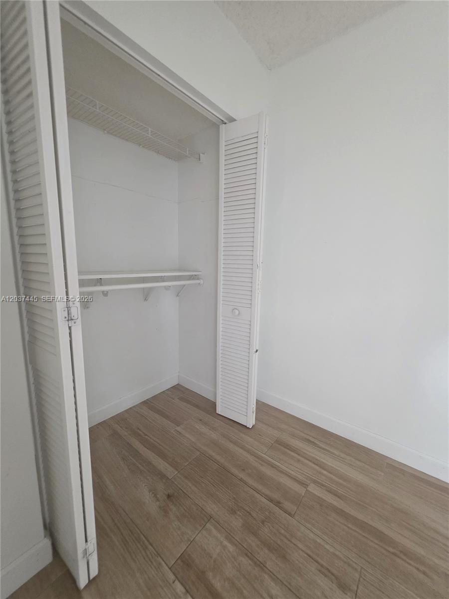 A closet with white louvered doors and wire shelving stands in a room with wood-look flooring — 15711 SW 137th Ave # 101, Miami FL 33177, MIAMI, FL
