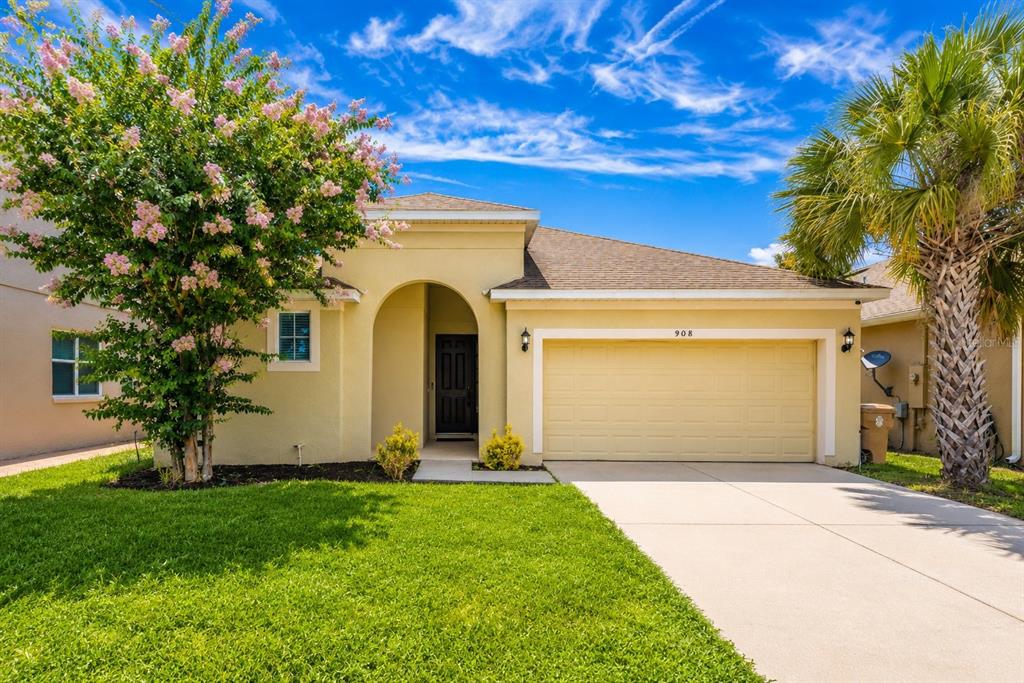 A single-story yellow house with a two-car garage, a front lawn, and a flowering tree — 908 MARISA LANE, KISSIMMEE, FL