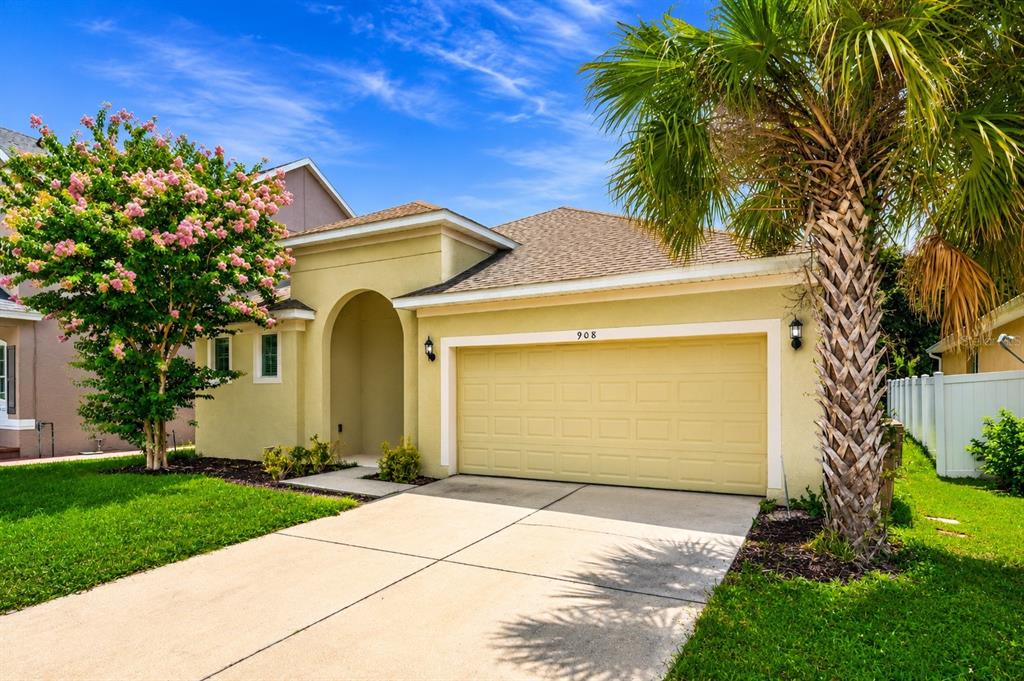 A single-story house exterior with a two-car garage, arched entryway, and palm tree at dusk — 908 MARISA LANE, KISSIMMEE, FL