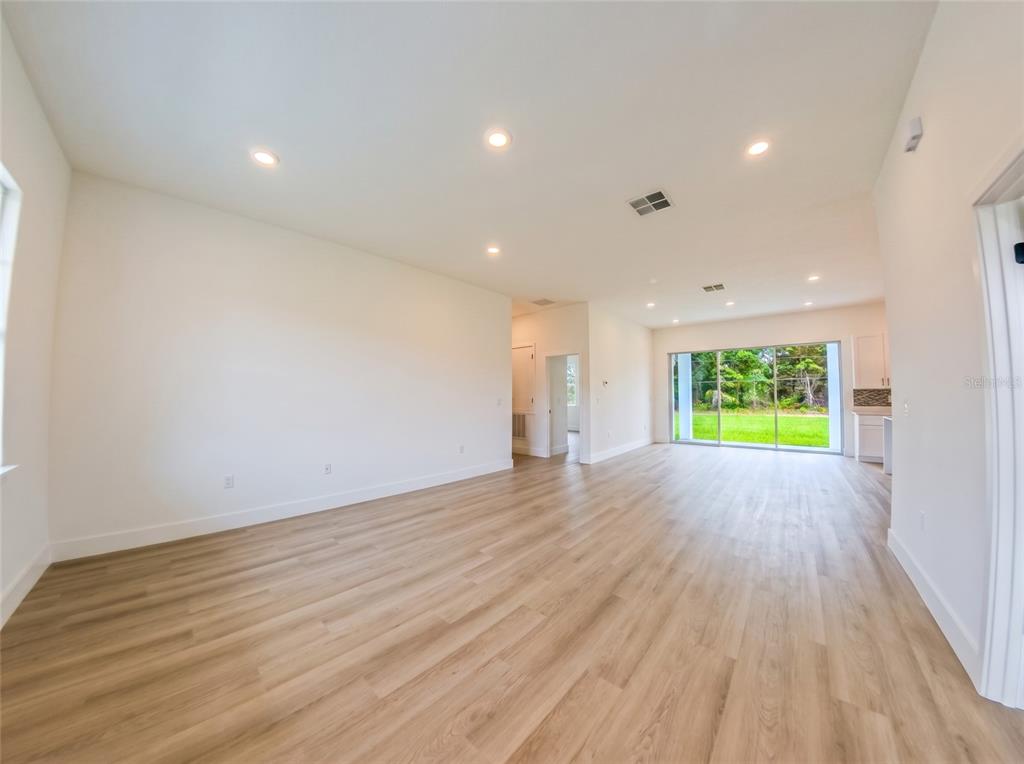 A bright, open-concept living area features light wood-look flooring, recessed lighting, and large sliding doors — 14144 SW 48TH COURT, OCALA, FL