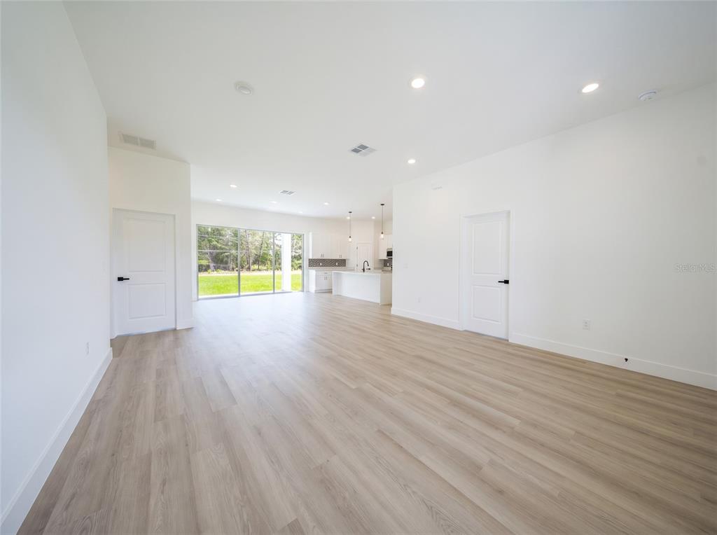 An open-concept living area features light wood-look flooring, white walls, and a kitchen beyond — 14144 SW 48TH COURT, OCALA, FL