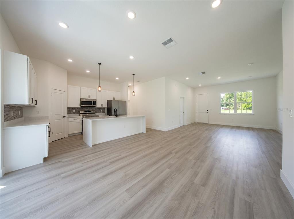 An open-concept kitchen and living area with white cabinets, stainless appliances, and light wood flooring — 14144 SW 48TH COURT, OCALA, FL