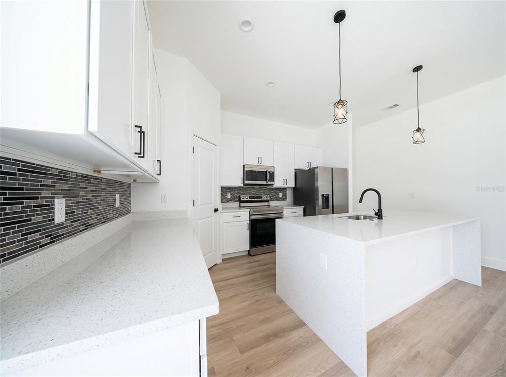A modern kitchen features white cabinets, quartz countertops, a tiled backsplash, and a central island — 14144 SW 48TH COURT, OCALA, FL