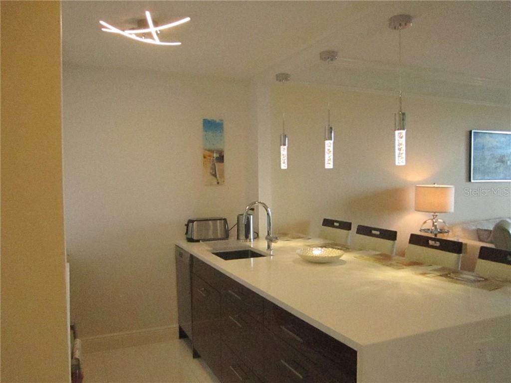 A modern kitchen island with a white countertop, sink, and dark wood cabinetry — 750 N TAMIAMI TRAIL UNIT 705, SARASOTA, FL