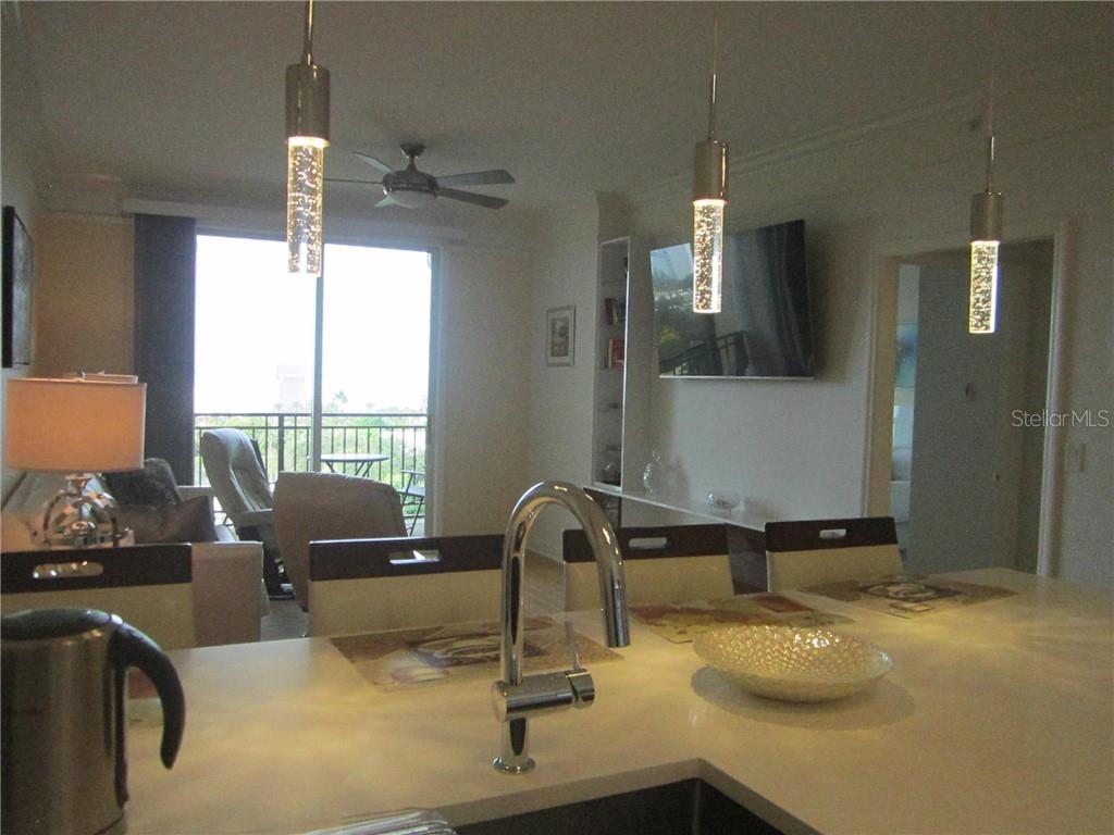A kitchen island with a sink overlooks a living area with a balcony and ceiling fan — 750 N TAMIAMI TRAIL UNIT 705, SARASOTA, FL