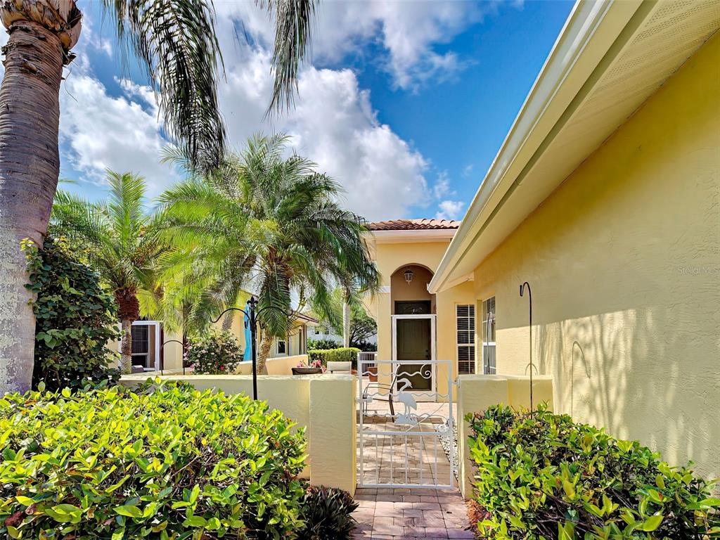A white metal gate leads to the front entrance of a yellow stucco home — 249 VISTA DEL LAGO WAY, VENICE, FL