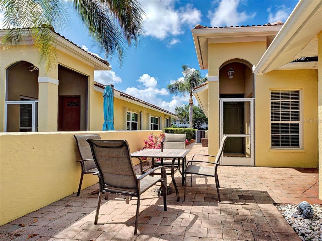 A paved patio features a dining set with four chairs against a yellow exterior wall — 249 VISTA DEL LAGO WAY, VENICE, FL