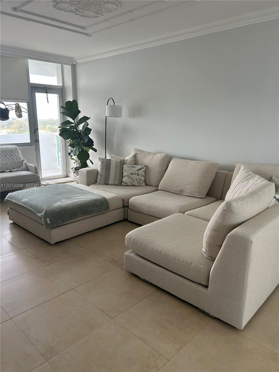 A living room features a large beige sectional sofa, tile flooring, and a glass balcony door — 7441 Wayne Ave # 7J, Miami Beach FL 33141, MIAMI BEACH, FL