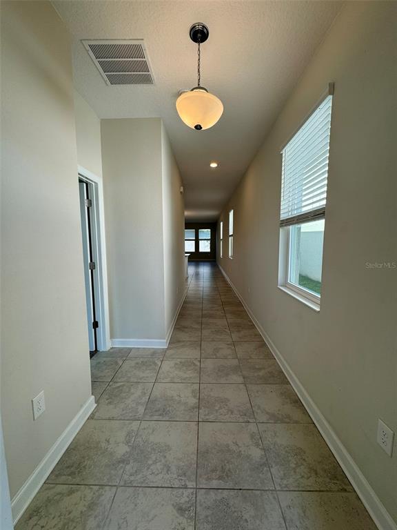 A long hallway with tiled floors, a pendant light, and a window with blinds — 14252 TITLE WAY, WINTER GARDEN, FL