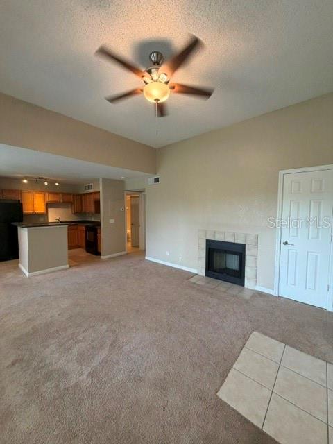 A living room with beige carpet, a ceiling fan, and a fireplace leads to a kitchen — 485 FORESTWAY CIRCLE UNIT 205, ALTAMONTE SPRINGS, FL