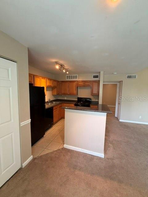A kitchen with wood cabinets, black appliances, and a breakfast bar overlooks a carpeted room — 485 FORESTWAY CIRCLE UNIT 205, ALTAMONTE SPRINGS, FL