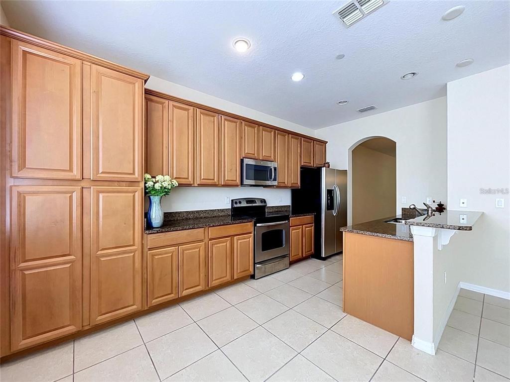 A kitchen features light wood cabinets, stainless steel appliances, granite countertops, and tile flooring — 10144 ARBOR RUN DRIVE UNIT 31, TAMPA, FL
