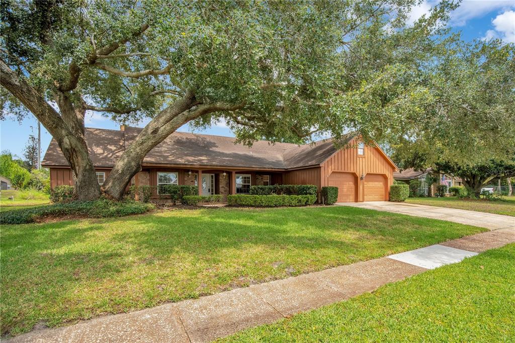 A single-story house with brown wood siding, a two-car garage, and large oak trees — 5307 JADE CIRCLE, ORLANDO, FL