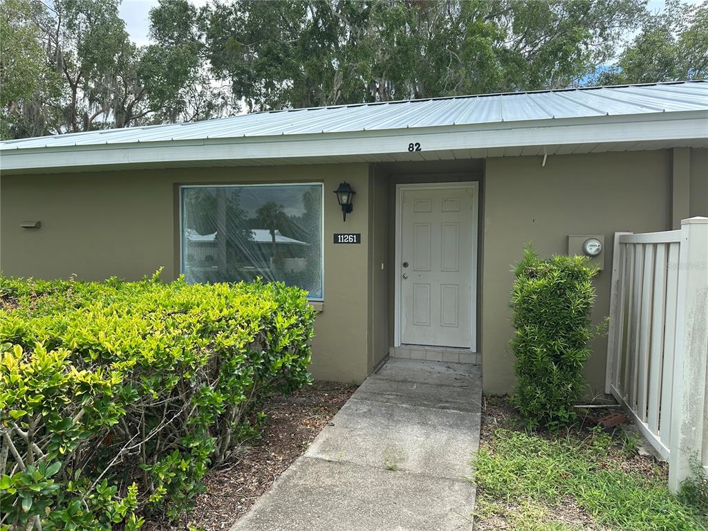 The exterior of a single-story home features a white door, large window, and metal roof — 11261 W BAYSHORE DRIVE UNIT 82, CRYSTAL RIVER, FL