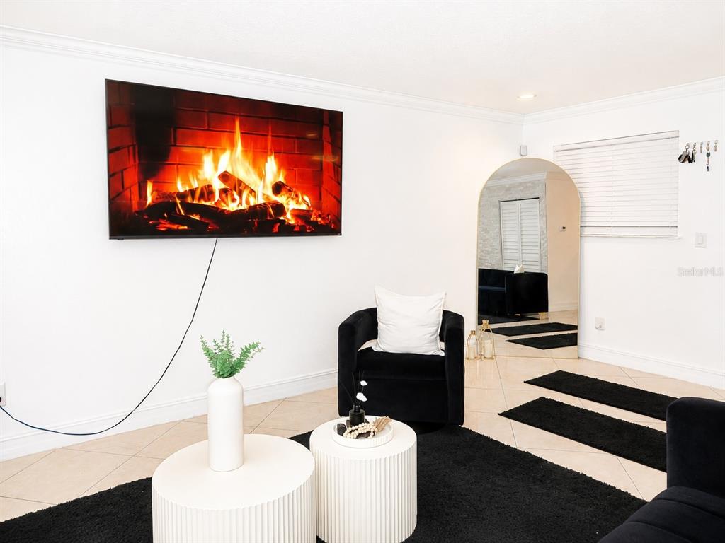 A living room features a wall-mounted television, a black armchair, and two white coffee tables — 7298 ULMERTON ROAD UNIT 307, LARGO, FL