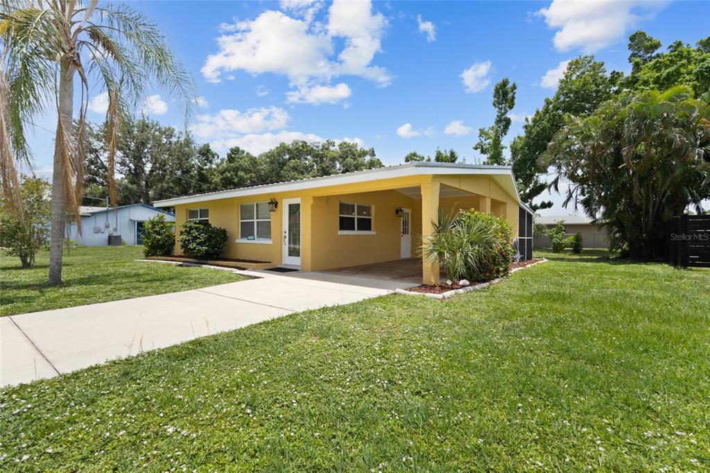 A yellow single-story house features a concrete driveway, a covered carport, and a grassy yard — 4065 ASBURY PLACE, SARASOTA, FL