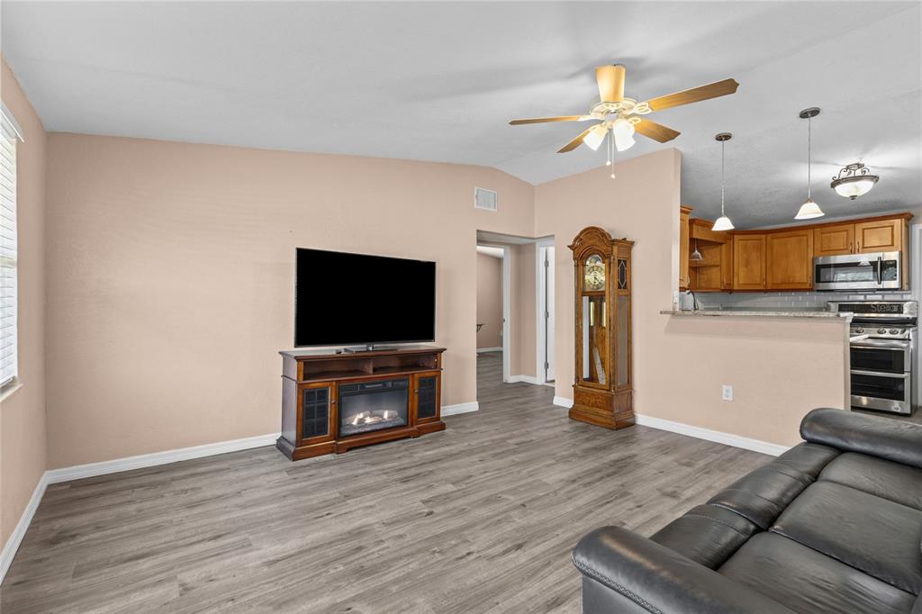 A living room with wood-look flooring, a television console, a grandfather clock, and an open kitchen — 4065 ASBURY PLACE, SARASOTA, FL