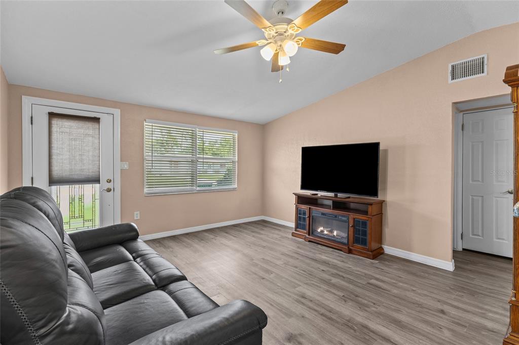 A living room features a grey sofa, wood-look flooring, a ceiling fan, and a television stand — 4065 ASBURY PLACE, SARASOTA, FL