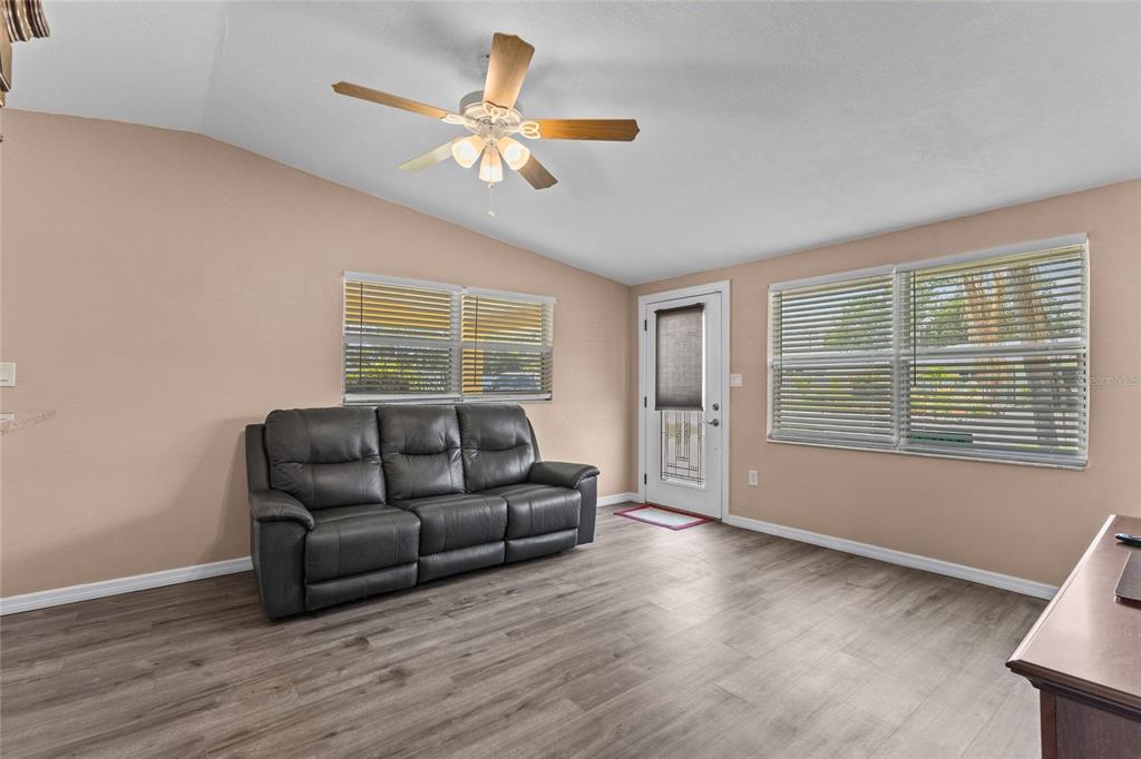 A living room features light-colored walls, wood-look flooring, a dark sofa, and a ceiling fan — 4065 ASBURY PLACE, SARASOTA, FL