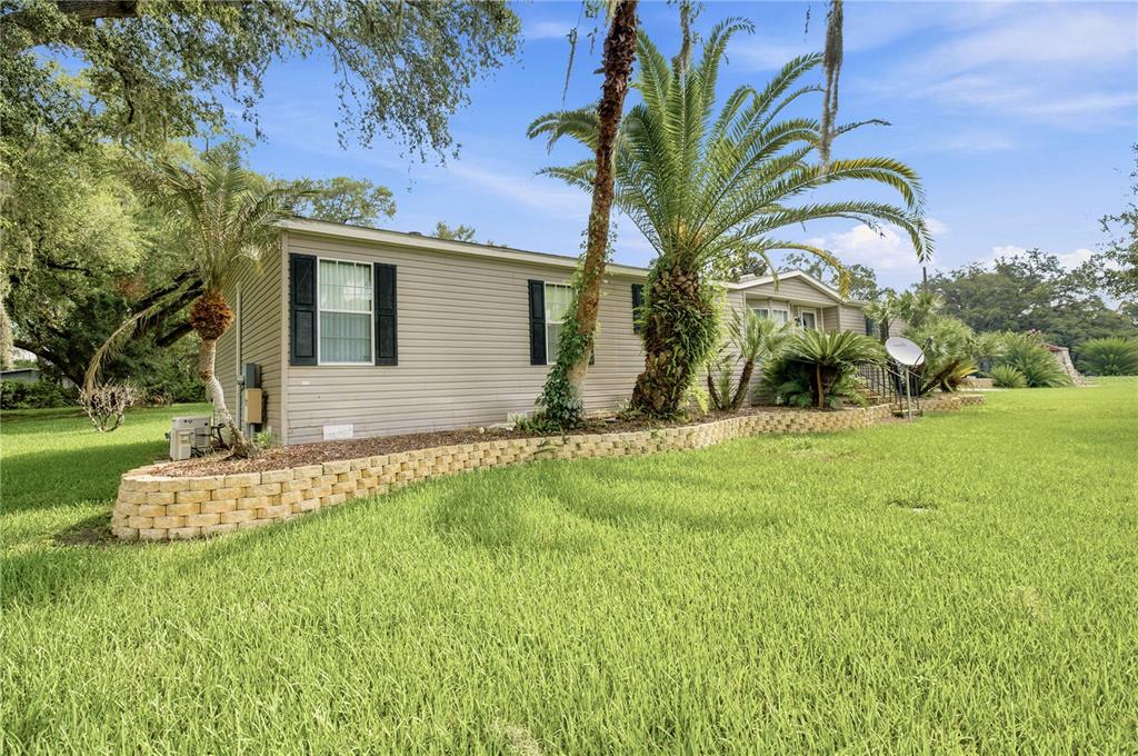 A light-colored manufactured home sits on a grassy lot with a stone retaining wall — 8420 COUNTY ROAD 109 A1, LADY LAKE, FL