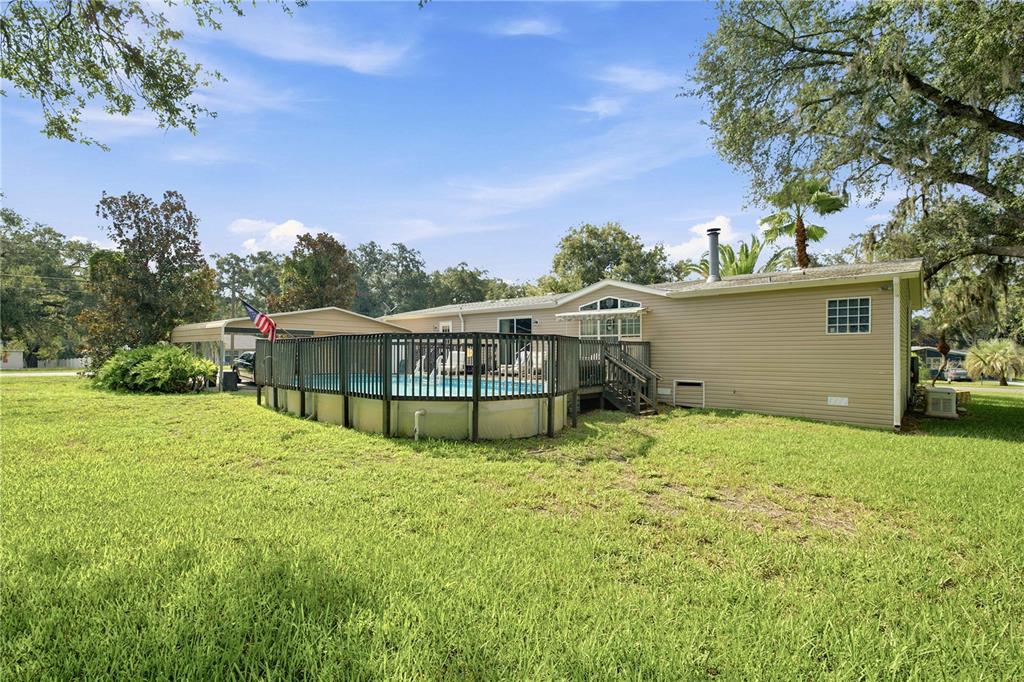 A beige mobile home features a large wooden deck surrounding an above-ground swimming pool — 8420 COUNTY ROAD 109 A1, LADY LAKE, FL