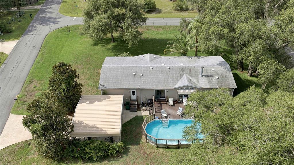 An aerial view shows a house with a carport, a wooden deck, and a swimming pool — 8420 COUNTY ROAD 109 A1, LADY LAKE, FL