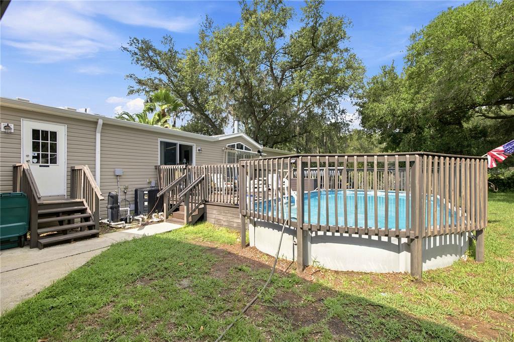 A beige house with a wooden deck and an above-ground swimming pool in the backyard — 8420 COUNTY ROAD 109 A1, LADY LAKE, FL