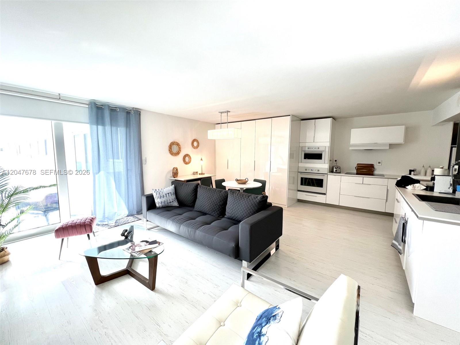 An open-concept living room and kitchen feature white cabinetry, light wood flooring, and modern furniture — 345 Ocean Dr # 525, Miami Beach FL 33139, MIAMI BEACH, FL
