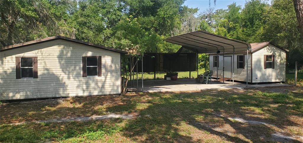 Two small light-colored buildings are connected by a large metal carport on a grassy lot — 18300 STATE ROAD 52, LAND O LAKES, FL