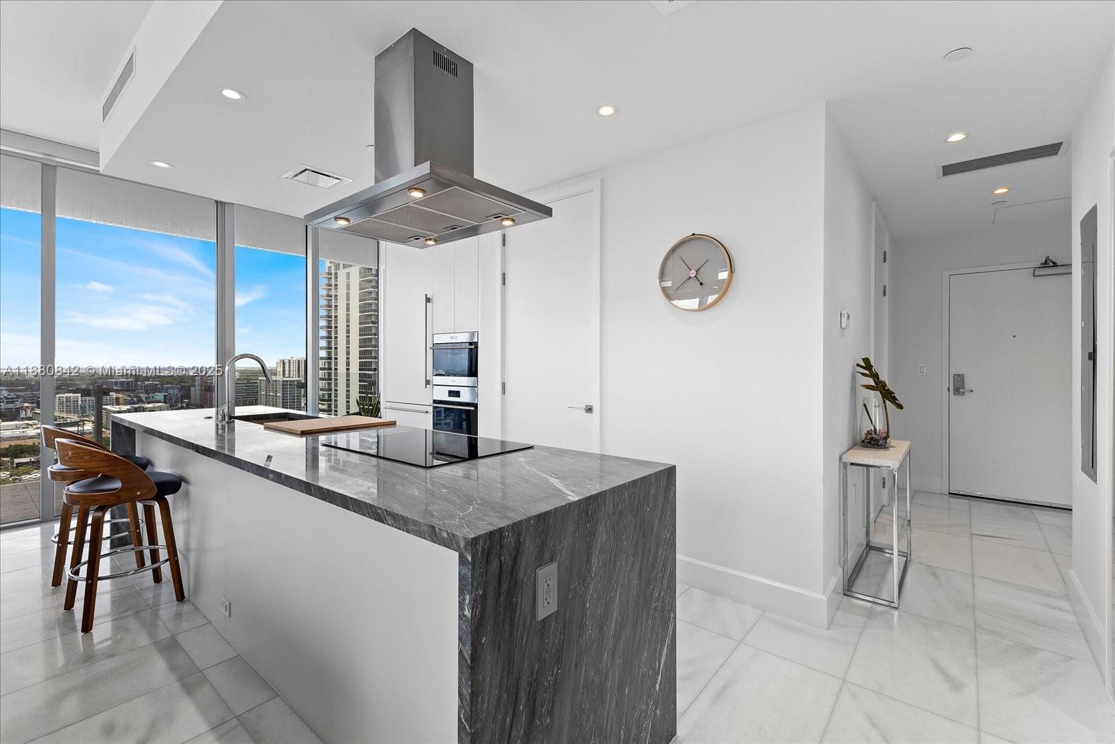 A modern kitchen features a marble waterfall island, stainless steel appliances, and floor-to-ceiling windows — 700 NE 26th Ter # 2605, Miami FL 33137, MIAMI, FL