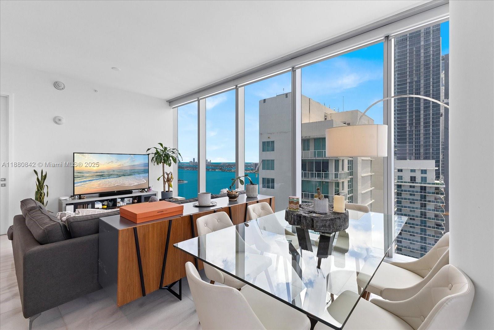 A modern living and dining area features floor-to-ceiling windows with views of the bay — 700 NE 26th Ter # 2605, Miami FL 33137, MIAMI, FL