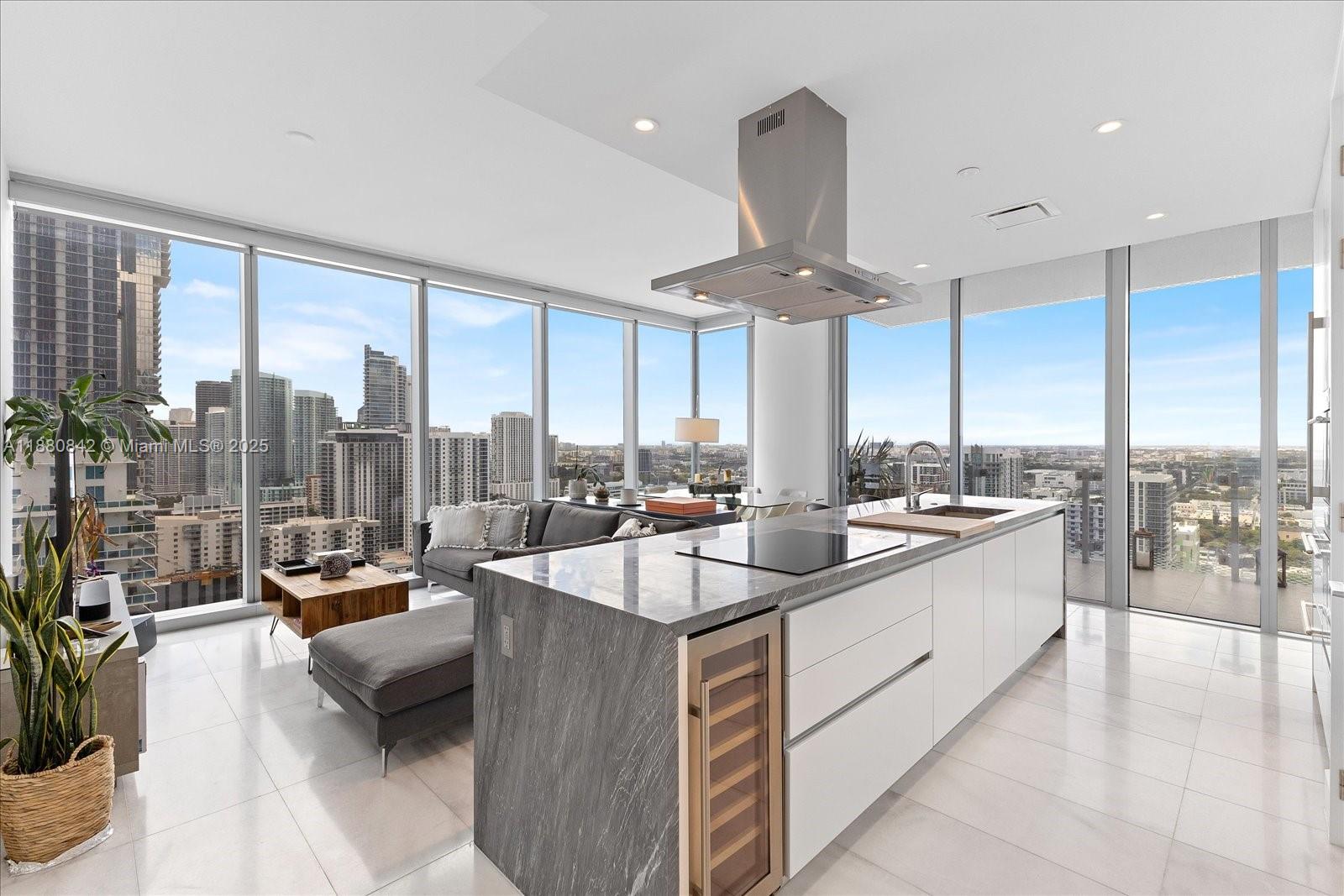 A modern kitchen island with a wine cooler sits in an open-concept apartment with floor-to-ceiling windows — 700 NE 26th Ter # 2605, Miami FL 33137, MIAMI, FL