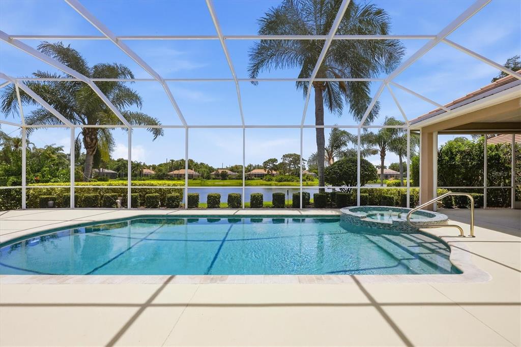 A screened-in swimming pool and spa overlook a lake with palm trees in the background — 8160 COLLINGWOOD COURT, UNIVERSITY PARK, FL