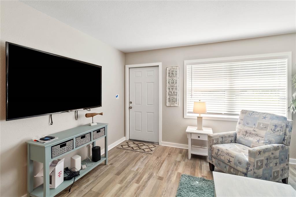 A living room features light wood-look flooring, a wall-mounted television, and a patterned armchair — 526 CONRAD ROAD, VENICE, FL